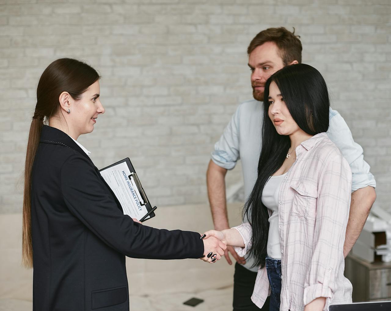 Professional business meeting with a handshake in an office environment featuring three adults in conversation.